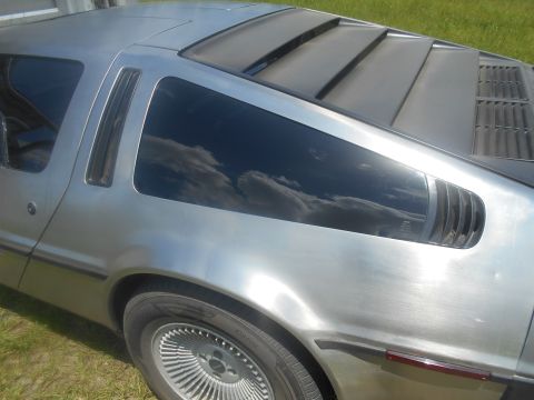 1992 Ford Bronco - Close-up view of the rear passenger side of a silver DeLorean DMC-12. The image shows the distinctive louvers on the rear window, the side…