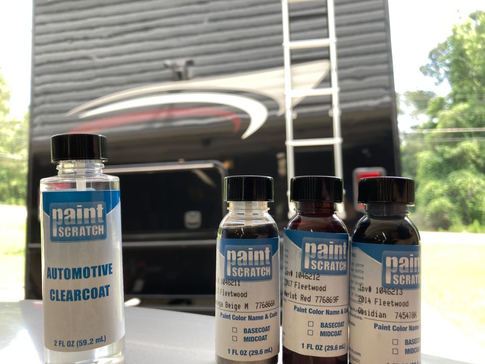 Four bottles of touch-up paint and automotive clearcoat in front of a black RV.