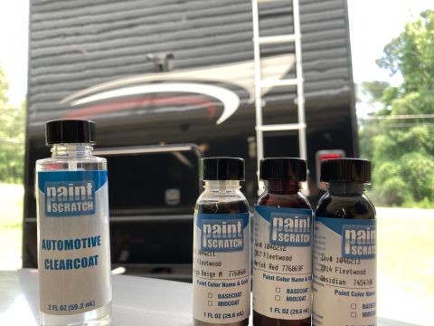 2015 Ford F-550 - Four bottles of automotive paint repair products are displayed in front of a large RV or motorhome. The bottles include clearcoat and three…