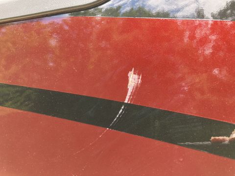 2015 Ford F-550 - A close-up view of a red vehicle's side panel shows a significant scratch across a black stripe. The scratch appears to have removed some o…