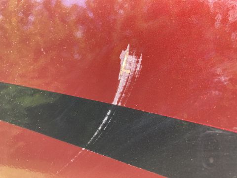 2015 Ford F-550 - A close-up view shows a scratch on the red metallic paint of a vehicle, with a black stripe running horizontally across the lower portion o…
