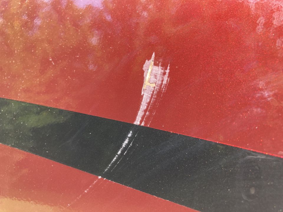 Close-up of a scratch on red metallic vehicle paint with a black stripe.