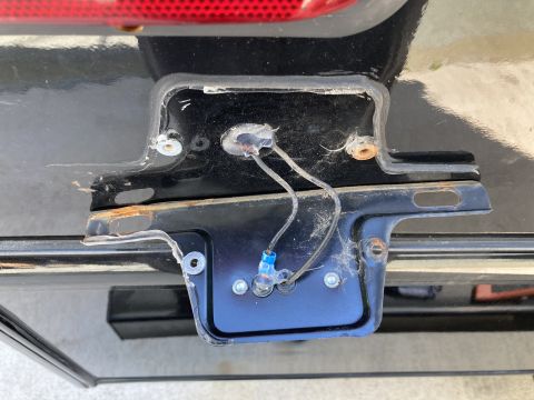2015 Ford F-550 - The rear of a black vehicle shows a rusted license plate bracket with exposed wiring and a blue wire connector. A portion of a red tailligh…