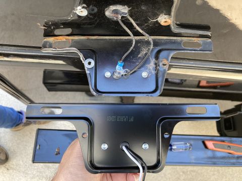 2015 Ford F-550 - A person is holding a black metal license plate bracket with a light attached. The bracket is positioned in front of a black metal surface…