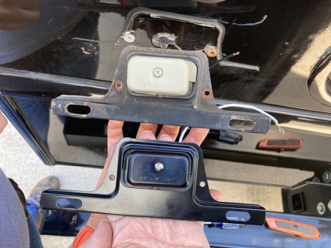 2015 Ford F-550 - A person holds a black license plate bracket with a light assembly below a rusted metal bracket with a light assembly attached to a black v…