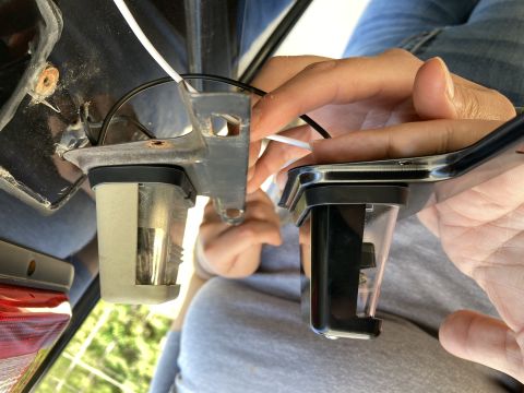 2015 Ford F-550 - A close-up view shows two license plate light housings being held. One housing is silver and appears to be older, while the other is black…