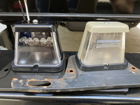2015 Ford F-550 - A new black LED license plate light assembly is shown next to an older, yellowed clear plastic license plate light assembly. Both are mount…