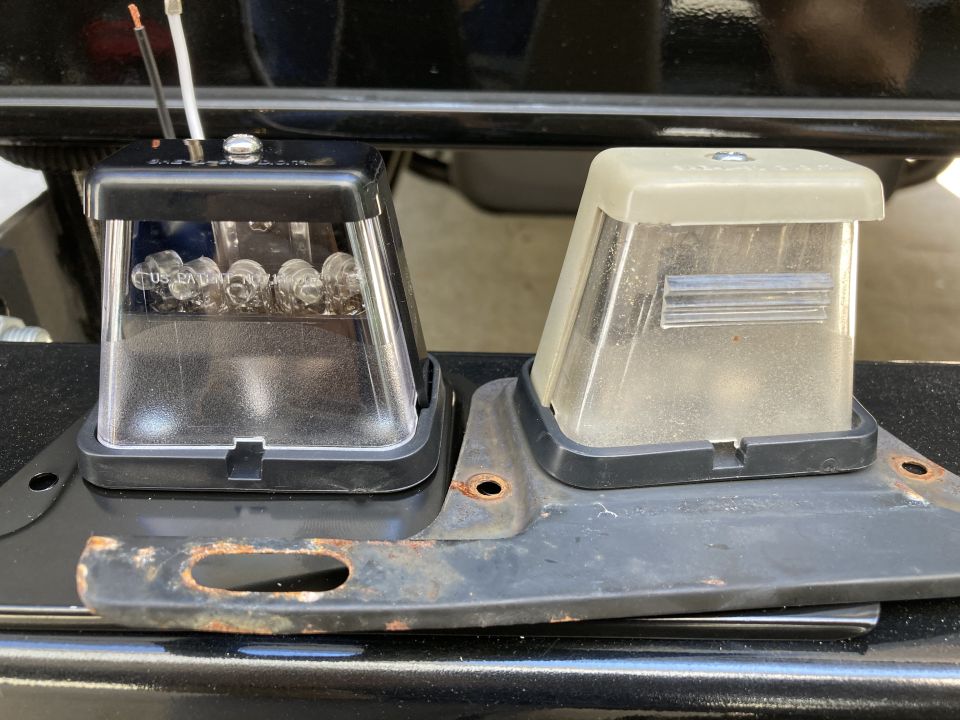 New black LED license plate light next to old yellowed clear license plate light on rusty bracket