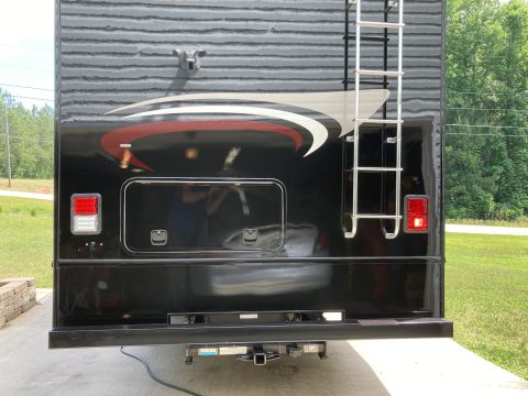 2015 Ford F-550 - The rear of a black RV is shown, featuring a silver ladder, red and white graphics, and two taillights. A trailer hitch is visible at the b…