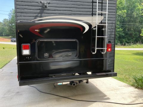 2015 Ford F-550 - The rear of a black RV with a chrome ladder attached to the back. A red and white graphic design is visible on the upper rear panel.