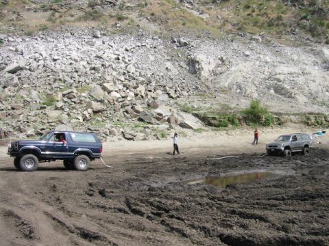 1985 Ford Bronco - Two off-road vehicles are stuck in thick mud at a rocky quarry site.