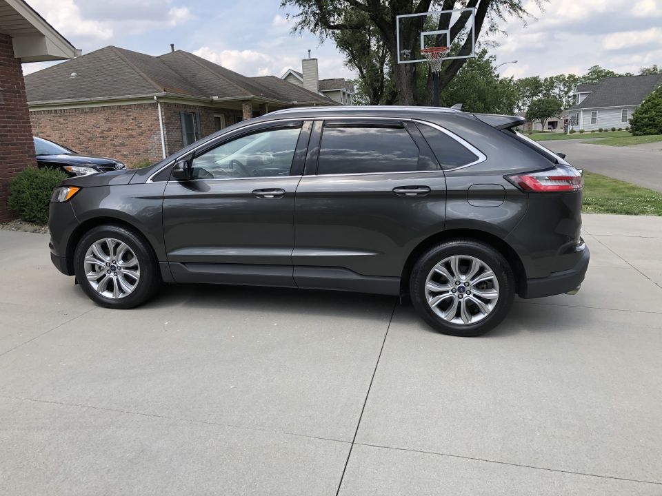 Dark gray Ford Edge SUV parked on a concrete driveway, side view