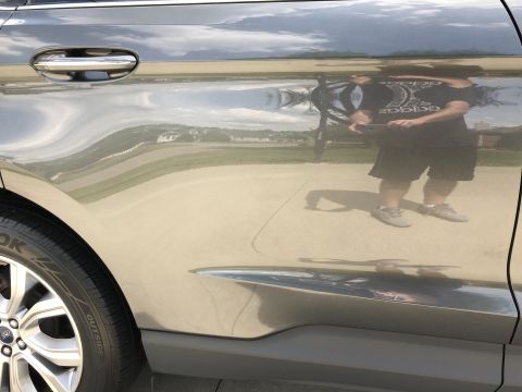 2019 Ford Everest - The reflection on the side of a gray SUV shows a person holding a phone and wearing a t-shirt and shorts. The vehicle's door handle and par…