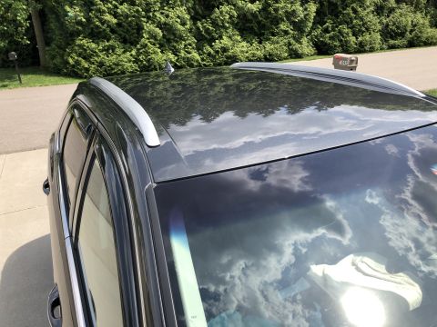2019 Ford Everest - A close-up, high-angle shot of the roof and hood of a dark gray SUV, reflecting a cloudy sky. Silver roof rails are visible along the top o…