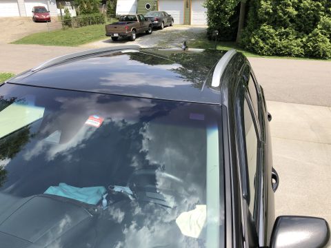 2019 Ford Everest - A dark gray SUV is parked on a paved driveway, viewed from a high angle looking down at the roof and windshield. Reflections of clouds and…
