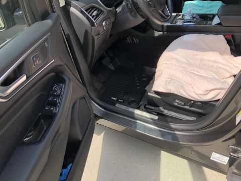 2019 Ford Everest - The interior of a dark-colored SUV is shown, focusing on the driver's side door and the front passenger seat. A tan blanket is draped over…