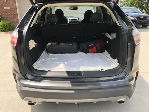 2019 Ford Everest - The open rear cargo area of a dark gray SUV is shown, with a white blanket covering the floor. A black toolbox and a red, blue, and black d…