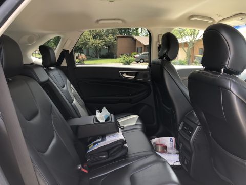 2019 Ford Everest - The interior of a black leather SUV, viewed from the rear passenger seats. A center console with a cup holder and a folded blanket are visi…