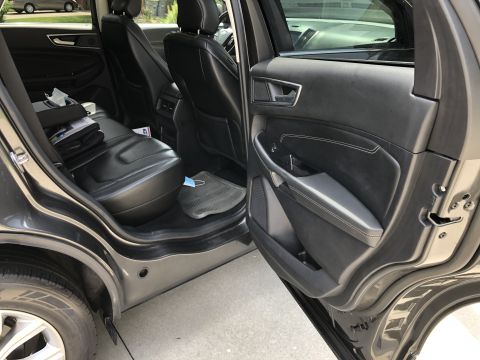 2019 Ford Everest - The interior of a dark-colored SUV is shown, focusing on the rear passenger seats and the driver's side door panel. A disposable face mask…