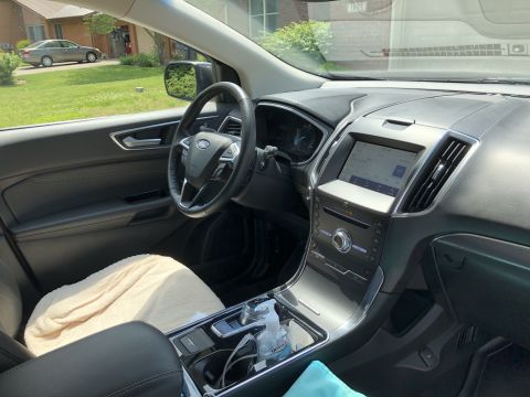 2019 Ford Everest - The interior of a Ford SUV shows the dashboard, steering wheel, and center console. A beige towel is placed on the passenger seat.