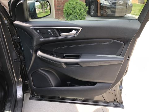 2019 Ford Everest - The interior driver's side door panel of a dark-colored vehicle is shown, featuring black leather upholstery with white stitching, a silver…