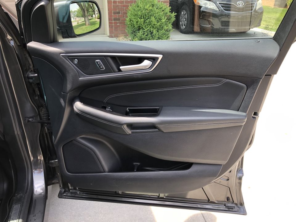 Interior driver's side door panel of a dark vehicle with black leather and white stitching.