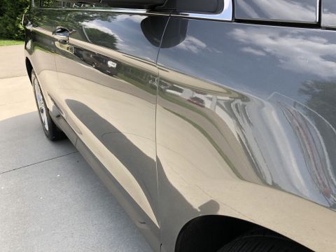 2019 Ford Everest - Close-up side view of a dark gray SUV reflecting the sky and surrounding environment. The vehicle's glossy paintwork highlights the curves…