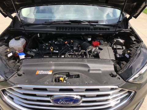 2019 Ford Everest - The open hood of a dark gray Ford SUV reveals the engine bay, with various components and the Ford logo visible on the front grille.