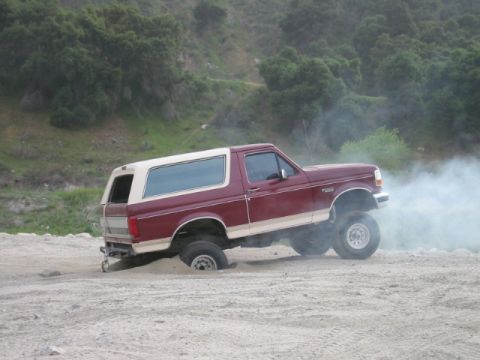 1985 Ford Bronco - This maroon and white Ford Bronco appears to be stuck in the sand, kicking up smoke as it struggles for traction.
