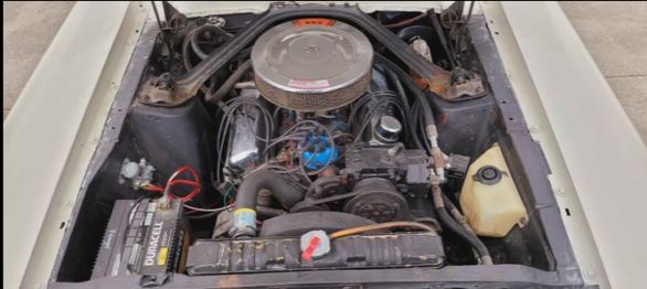 Engine bay of a classic car, showing air cleaner, carburetor, distributor, battery, and radiator.