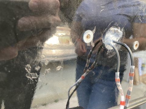2015 Ford F-550 - A close-up view shows three black wires with red and white connectors passing through a hole in a dark, reflective surface. Two metal washe…