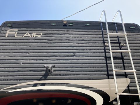 2015 Ford F-550 - The rear of a black RV motorhome with a ladder attached to the right side. The word "FLAIR" is visible in silver lettering on the upper rea…