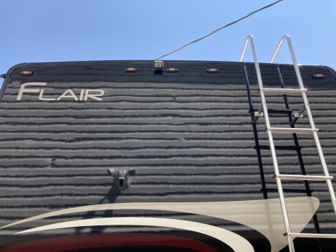 2015 Ford F-550 - The rear of a black RV with a ladder attached to the roof. The RV has "FLAIR" text on the upper rear and a backup camera is visible.