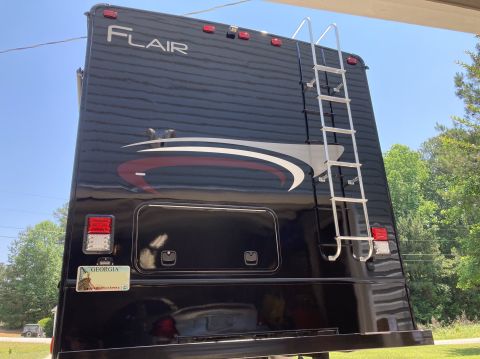 2015 Ford F-550 - The rear of a black Fleetwood Flair RV is shown parked outdoors on a sunny day. A silver ladder is mounted to the back of the RV, and a Geo…