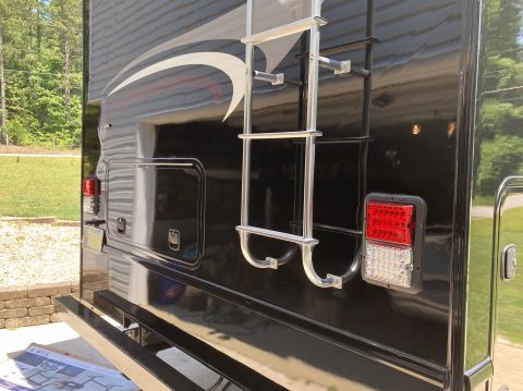 2015 Ford F-550 - The rear of a black RV is shown, featuring a silver ladder, a red and white LED taillight, and storage compartments. A black bumper bar is…