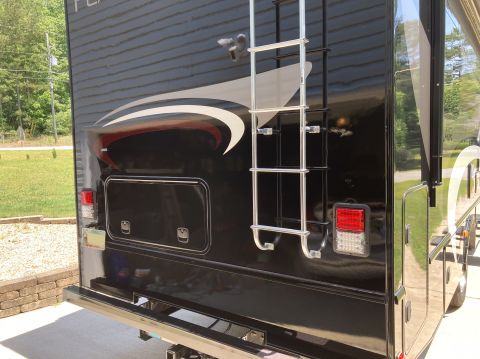2015 Ford F-550 - The rear of a black RV is shown, featuring a chrome ladder, a red and white tail light, and storage compartments. A decorative graphic with…