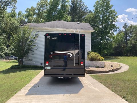2015 Ford F-550 - The rear of a black Fleetwood RV is parked on a concrete driveway in front of a house. The RV has a ladder attached to the back and the wor…