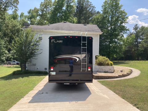 2015 Ford F-550 - The rear of a black Fleetwood Flair motorhome is parked on a concrete driveway in front of a house. A silver ladder is mounted to the rear…