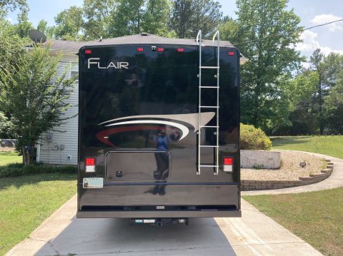 2015 Ford F-550 - The rear of a black Fleetwood Flair motorhome is shown parked on a concrete driveway in front of a house. A silver ladder is mounted to the…
