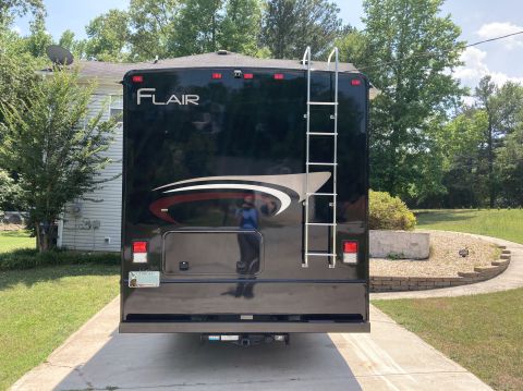 2015 Ford F-550 - The rear of a black Fleetwood Flair motorhome is shown parked on a concrete driveway. A silver ladder is mounted to the rear of the vehicle…