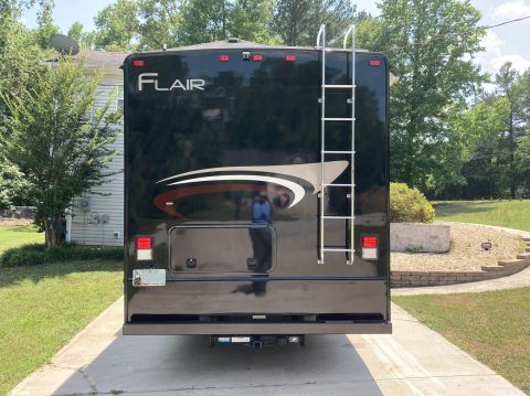 2015 Ford F-550 - The rear of a black Fleetwood Flair motorhome is shown parked on a concrete driveway. A ladder is mounted to the rear of the vehicle, and a…