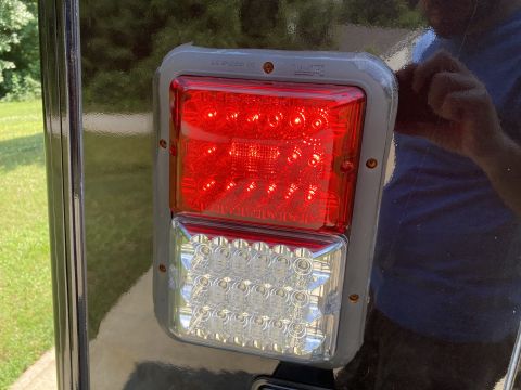 2015 Ford F-550 - A close-up view of a red and clear LED trailer light assembly mounted on the rear of a dark-colored vehicle. The light assembly has a gray…