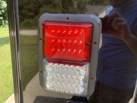 2015 Ford F-550 - A close-up view of a red and clear LED trailer tail light assembly mounted on a dark, glossy vehicle surface. The assembly has a gray rubbe…