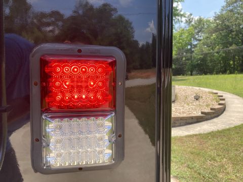 2015 Ford F-550 - A close-up of a red and clear LED trailer light assembly mounted on the dark, reflective side of a vehicle. The background shows a curved c…