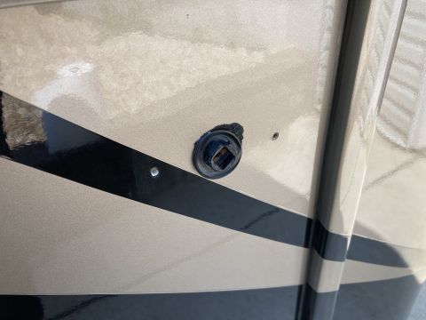 2015 Ford F-550 - A close-up view of a black square receptacle with a metal insert, mounted on the tan and black striped exterior of a vehicle. Two small sil…