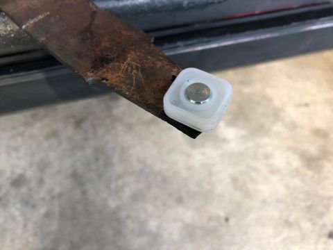 1978 Ford Bronco - A close-up shows a rusty metal bracket with a white plastic roller and a silver metal pin attached to its end.