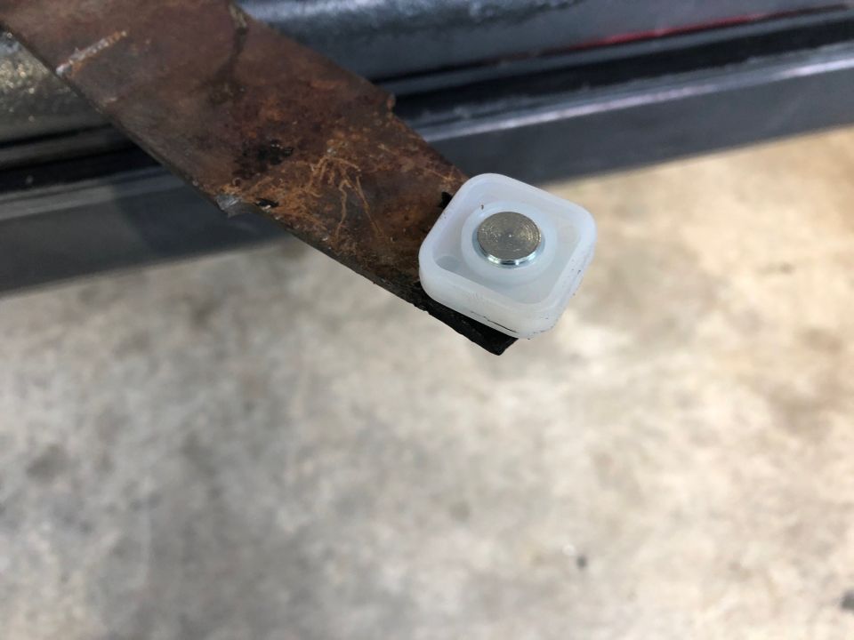 Close-up of a rusty metal bracket with a white plastic roller and silver pin.
