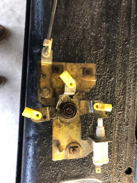 1978 Ford Bronco - A close-up view of a yellow metal door latch mechanism with yellow plastic clips and a black coiled spring, mounted on a textured black sur…