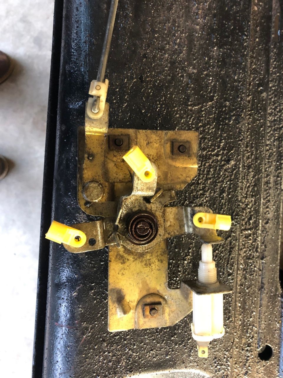 Yellow door latch mechanism with yellow clips and spring on black surface.