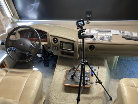 2015 Ford F-550 - Interior view of a motorhome's cockpit, showing the driver's seat, steering wheel, and dashboard. A tripod with a camera is set up in the p…